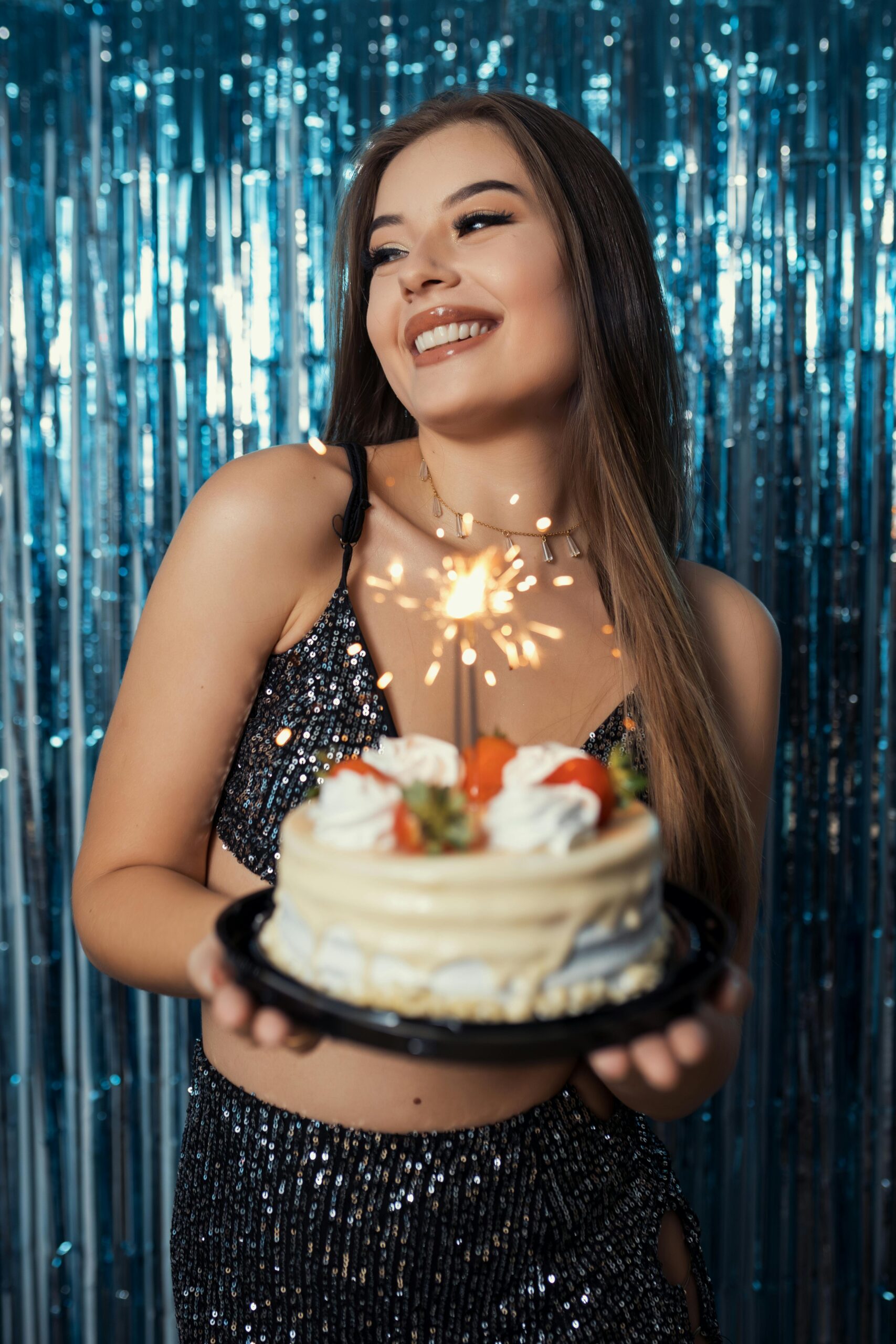 Young woman joyfully holding a cake with sparkler at a birthday party in Brazil.